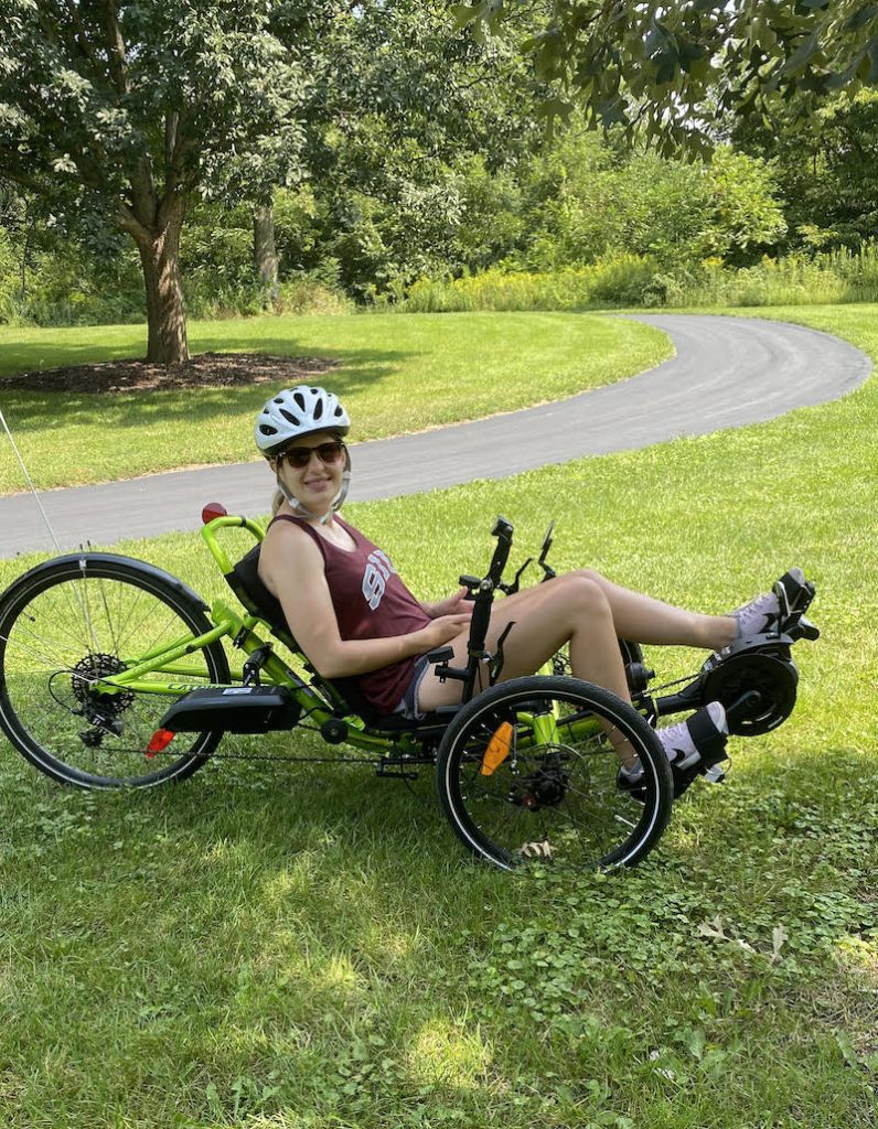 A white woman wearing a helmet and riding a recumbent bike on a sunny day.