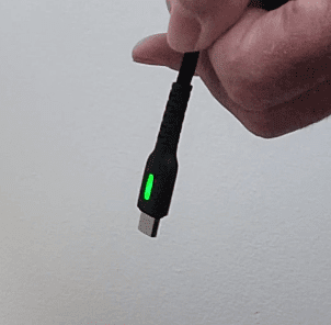 A hand holding the end of a charging cable with a green light on it