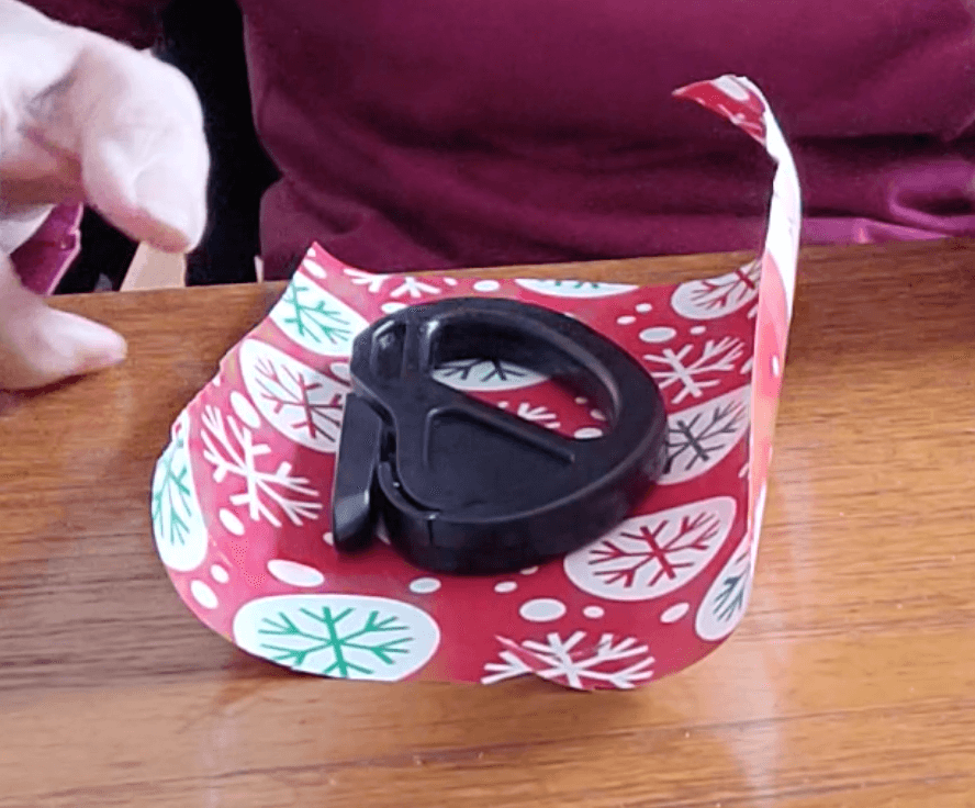 The black gift wrap cutter is on its side on top of a small piece of wrapping paper. It has a relatively large handle and the blade is not visible.