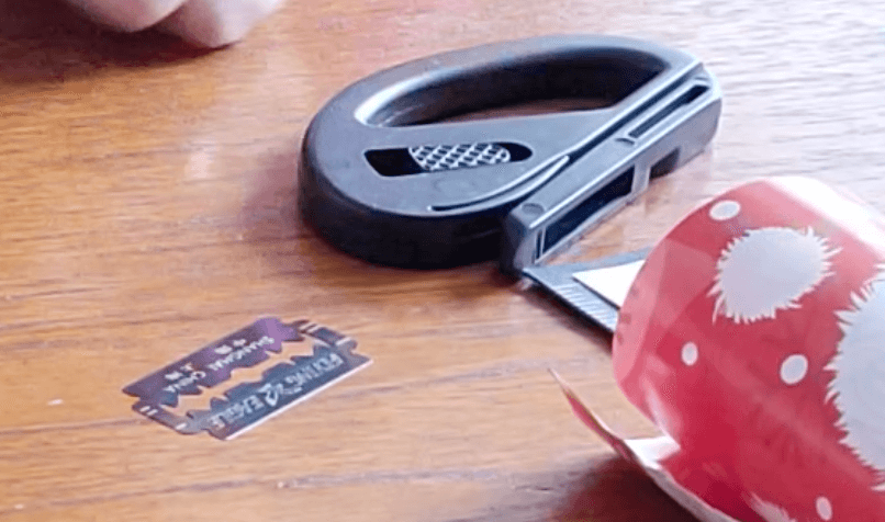 The black gift wrap cutter on its side on a table. Beside it is the blade sitting on the table.