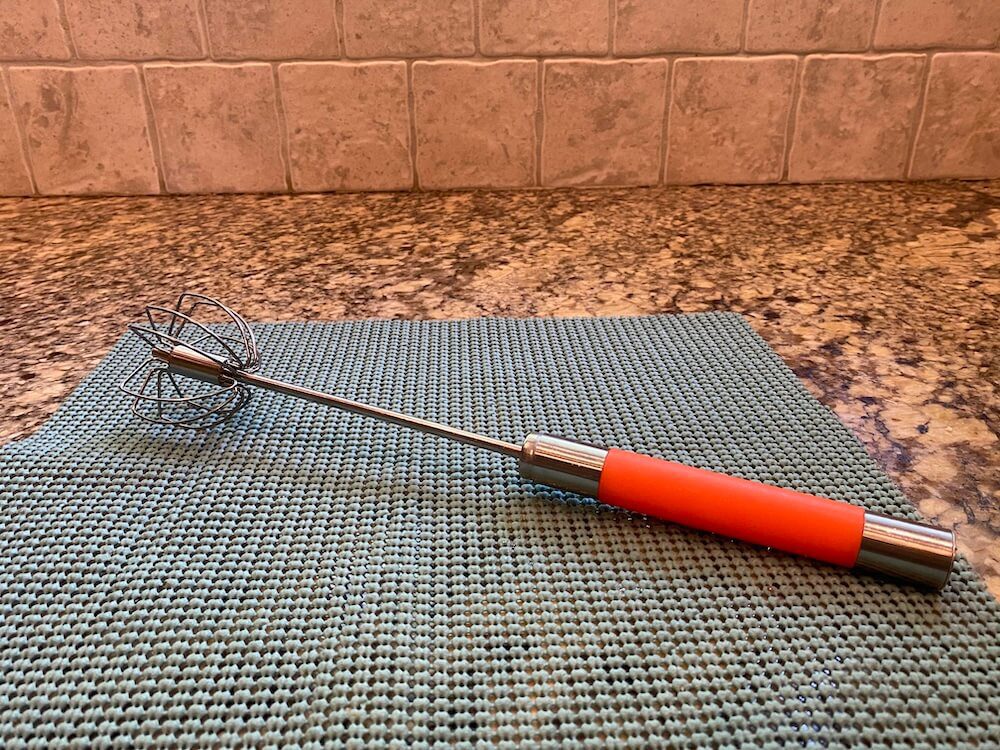 The metal whisk with a red handle, on a kitchen counter