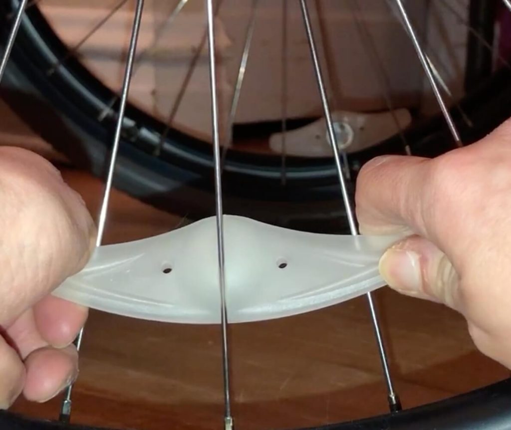 A person is attaching the light to the spoke using both hands. There is a small slit to that you pull the spoke into.