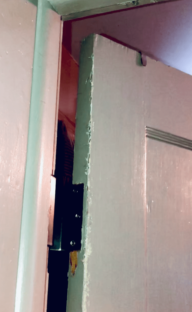 Swing clear door hinge attached to white door and frame. There is more distance between the door and the frame than with a standard hinge.