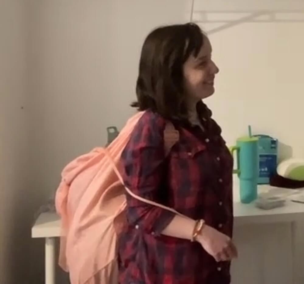 A side view of a neon orange laundry backpack. Thee person has pulled the drawstring around to the front and is holding it in her hand.