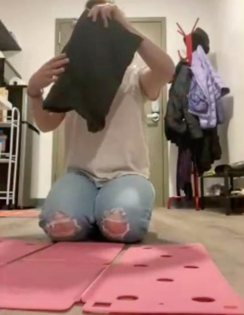 A person is holding up the neatly folded shirt. The pink FlipFold is laying out flat on the floor.