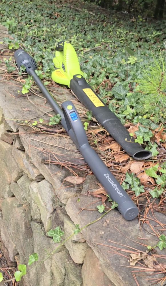 Full length shot of ZoomBroom laying beside a cordless, traditional leaf blower that has is bulkier at the handle.