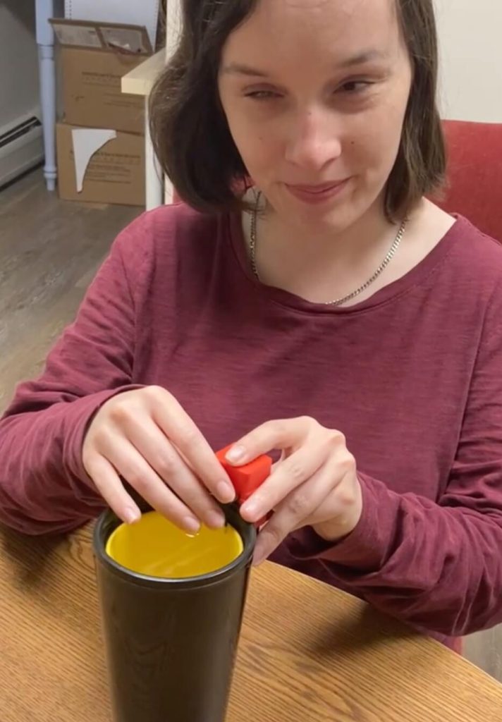 Hannah sits at a table and puts the indicator on the side of a glass of water