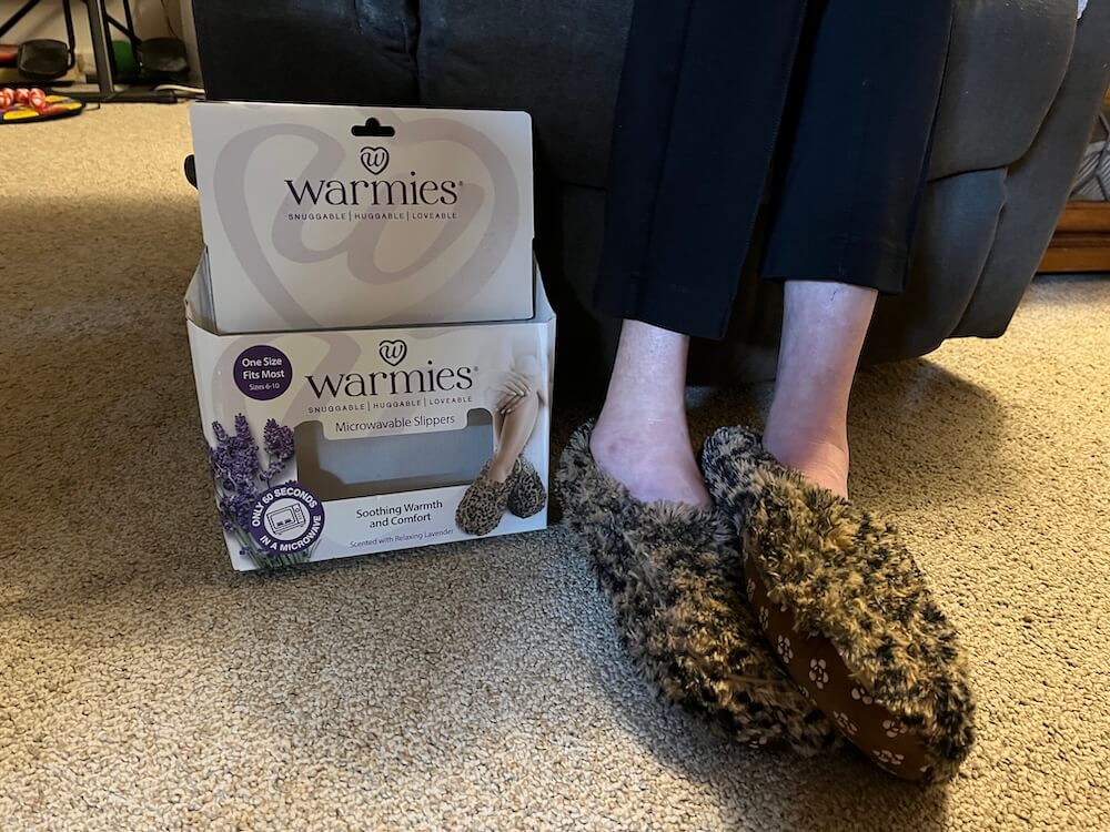 A person wearing the slippers in a lounge chair with the packaging sitting beside their feet.