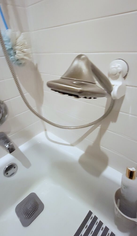 View of the silver shower head attached to a lower spot on the wall, hanging over the middle of the bathtub.