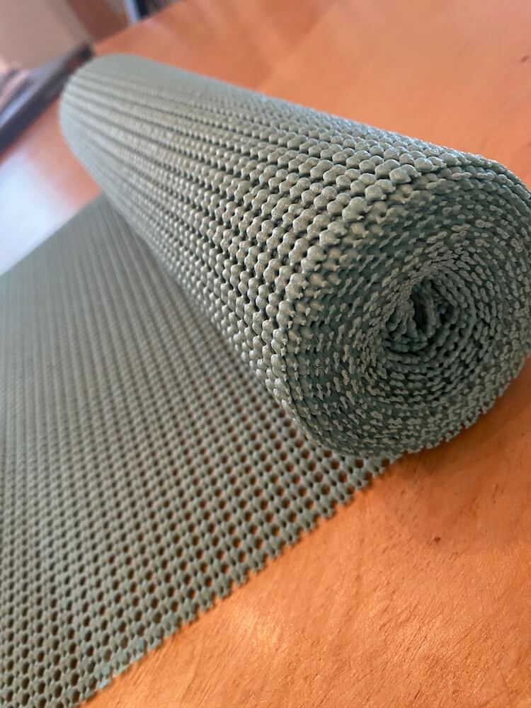 A roll of teal shelf liner unrolling on a wooden table.