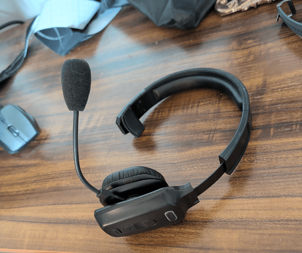 A black headphone set with a microphone laying on a wooden desktop.