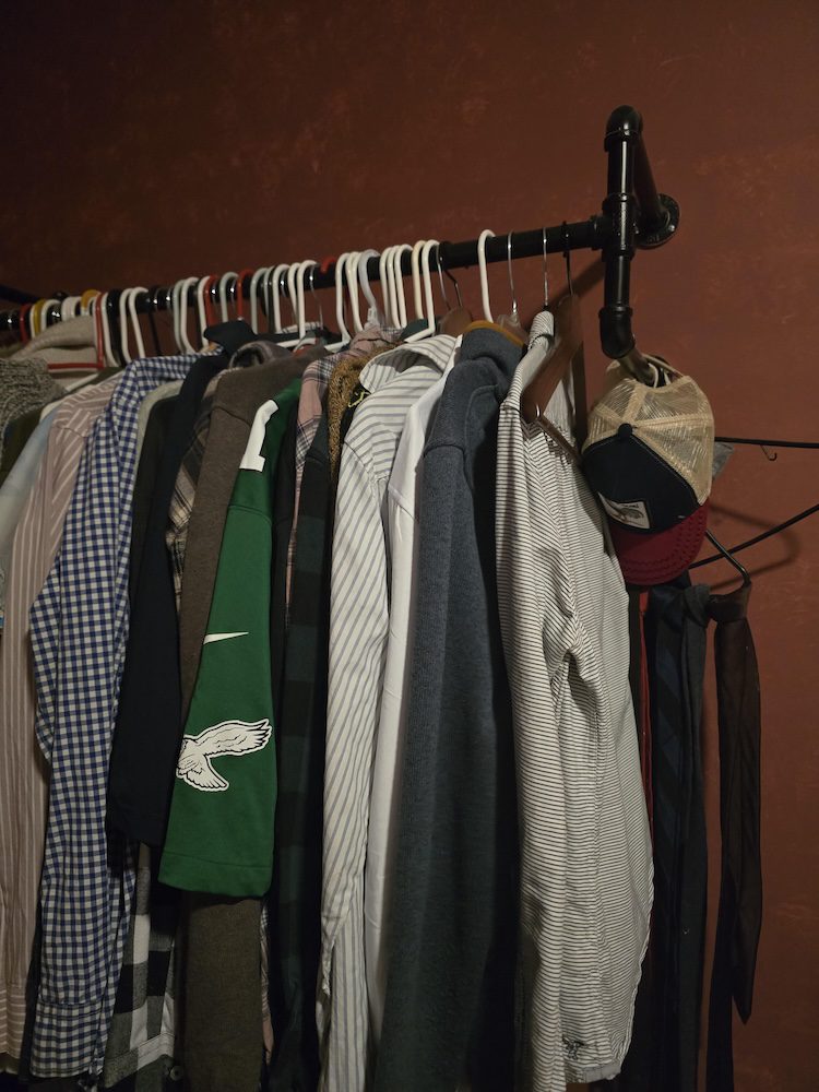 Clothes on hangers, hanging from a black clothing rail screwed into a red wall.