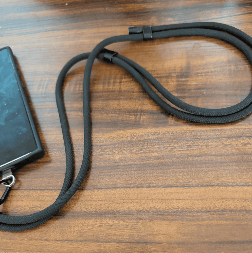 A black rope-like lanyard attached to a cell phone, on a wooden desk top.